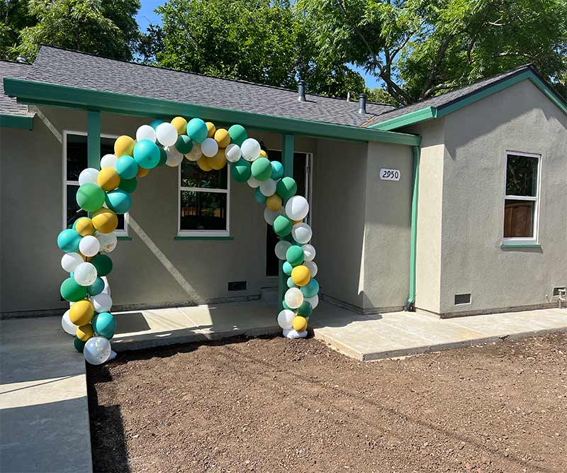 residential property with green, yellow, and white balloons in an arch shape